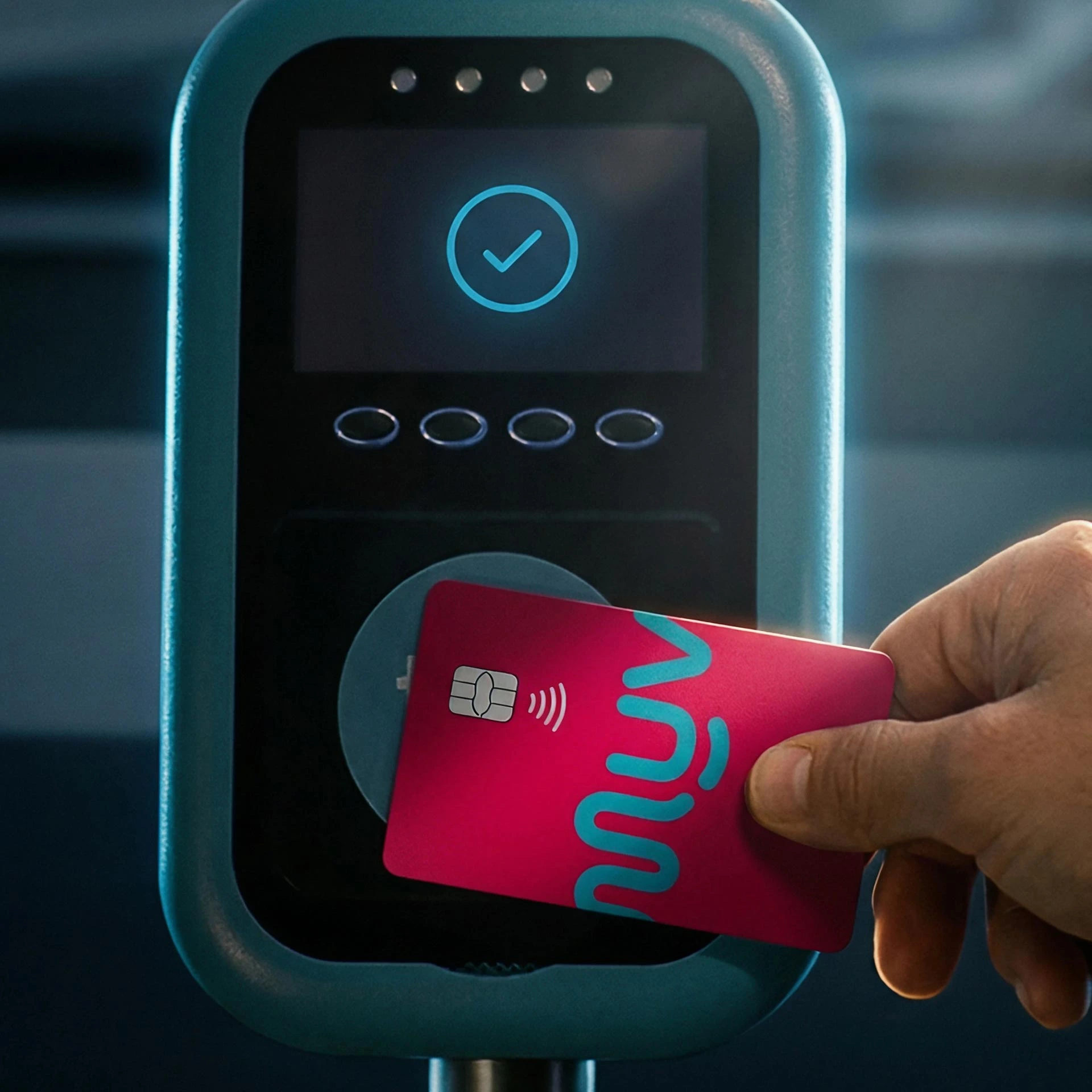 Hand holding a pink contactless card near a scanner showing a blue checkmark on screen.