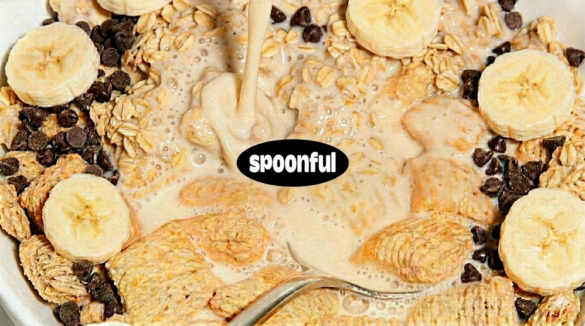 Milk being poured over cereal with banana slices and chocolate chips in a white bowl.