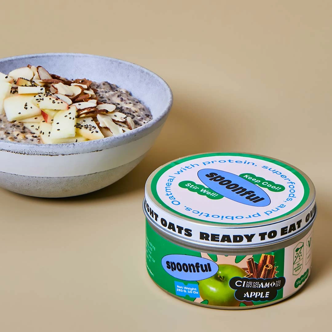 Bowl of oatmeal with apple slices, almonds, chia seeds next to cinnamon apple flavored Spoonful oatmeal container.